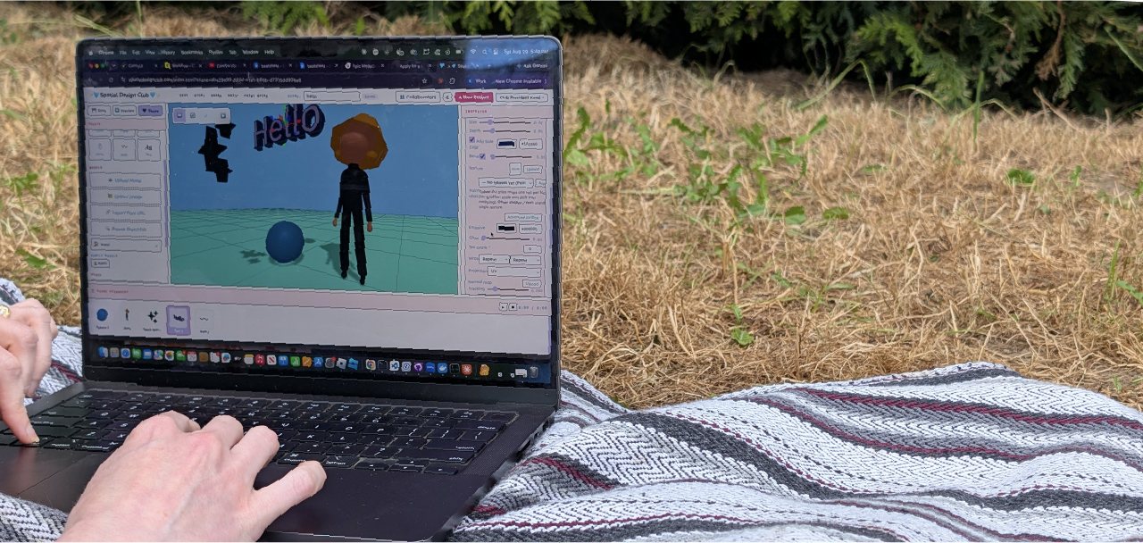 Editing a scene with 3D Hello text and an avatar in the SDC editor, on a laptop outdoors on a woven blanket